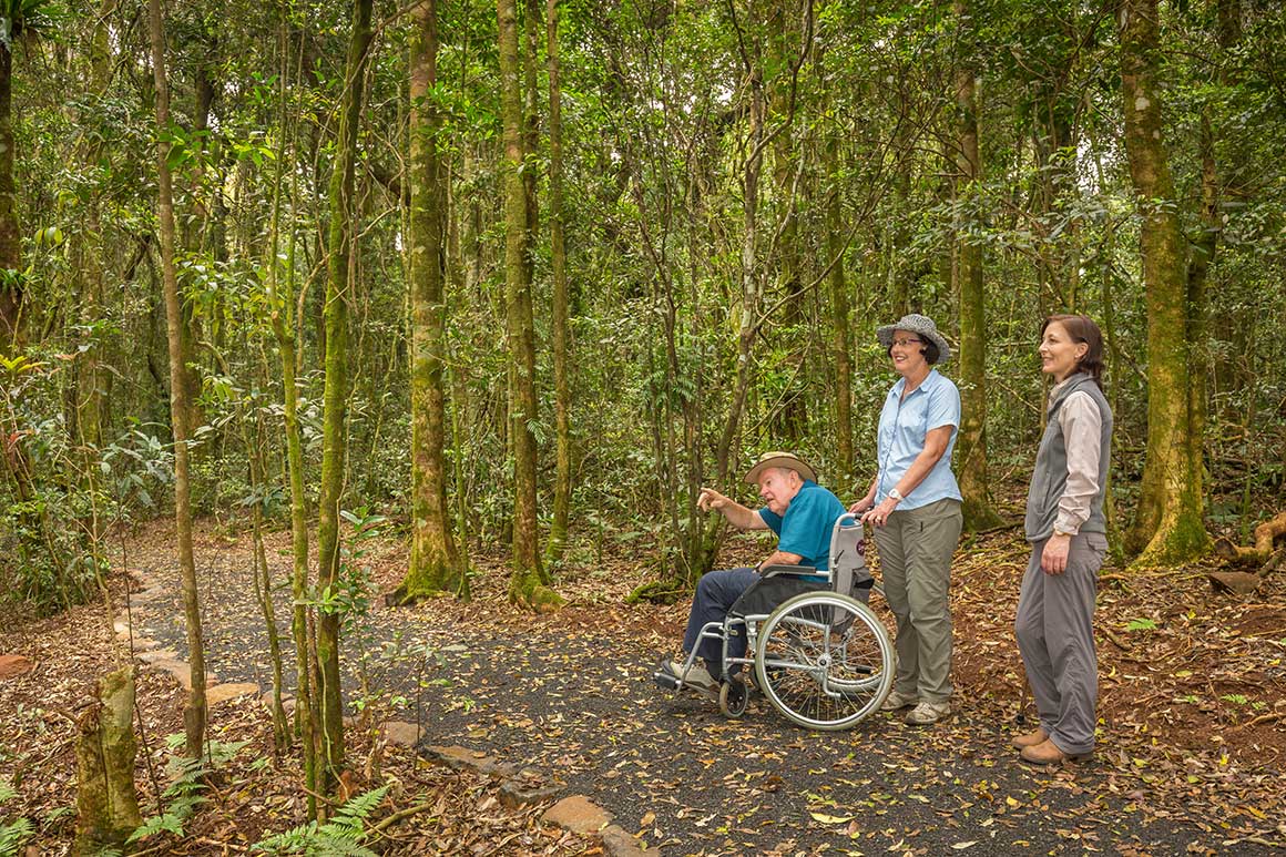 Three adults, two standing and one in a wheelchair, venture along a sealed track.