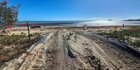 Black track matting laid over sandy dune going down to a beach and ocean in the background.