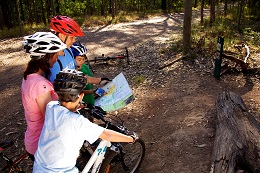 Photo of family of mountain-bike riders stopped on the side of a trail reading a map.
