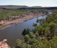 View from lookout looking down at river with vegetation missing from the riverbank edge. Red gorge cliffs in the background