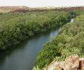 View from lookout looking down at river with lush green vegetation growing right up to riverbank edge. Red gorge cliffs in the background