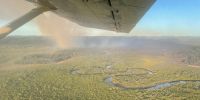 An ariel view of a planned burn on K’gari. Brown smoke rises from the rainforest, nearby a winding creek.  