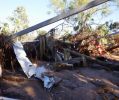 Shelter with no roof and signs missing. Shelter floor covered in mud, twisted metal and vegetation debris