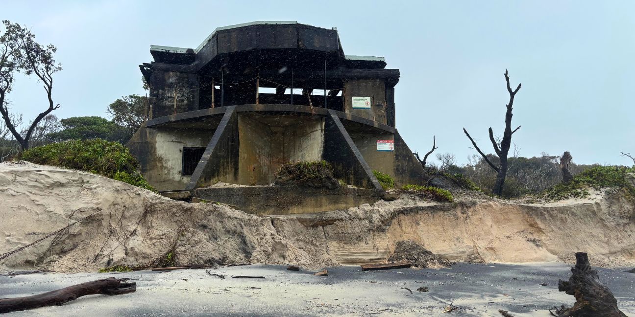 Concrete gun emplacement building perched on an eroding sand dune.