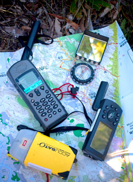 Photo of a satellite phone, compass and mobile phone sitting on top of a map.