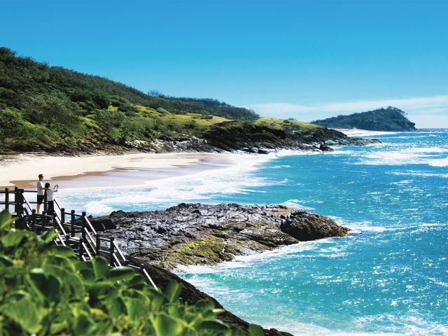 Sand dunes cloaked in vivid green curve to a K'gari-blue ocean.