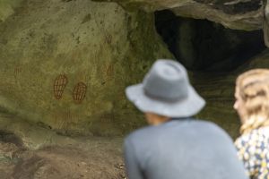 Two visitors gaze at rock art in cave.