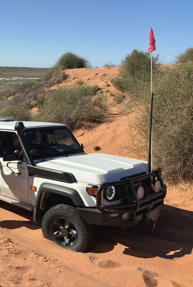 Photo of high clearance 4WD, driving on a dune with a high visibility flag.