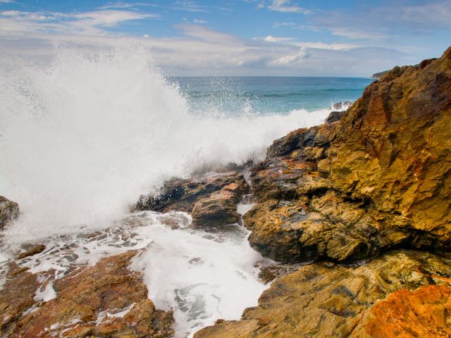 The rocky headland at Honeymoon Bay is coloured with orange and yellow hues.