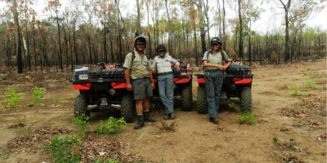 Three Rangers in uniform leaning against quad bikes and smiling at the camera