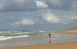 Beach landscope with a solo person fishing at the shore.