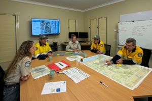 Photo of rangers strategising over maps and planning documentation for planned burns in a meeting operations room.