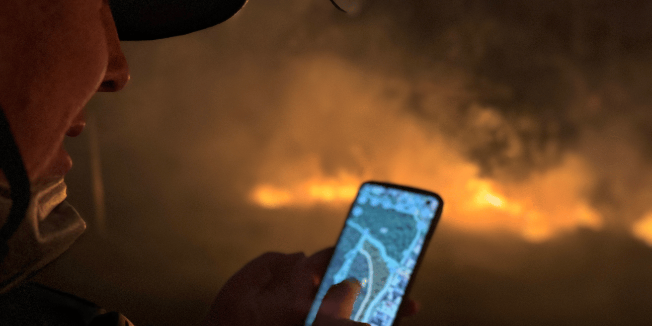 Close up of Rangers face holding a mobile phone with fire burning in the background.
