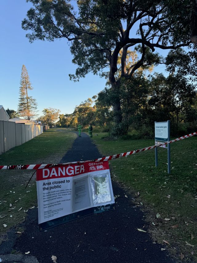 Photo of park closure sign across pathway with firefighting rangers in background