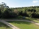 Photo of the Settlement picnic area as it is now—a large grassy area bounded by forest, with a timber information shelter and the start of a walking track