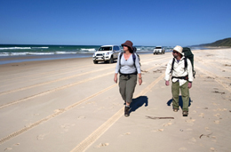 Photo of two walkers on the beach with a 4WD driving alongside them.