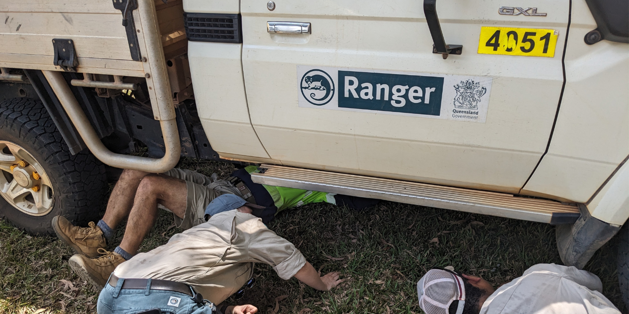 Three people crouching, looking under Ranger vehicle