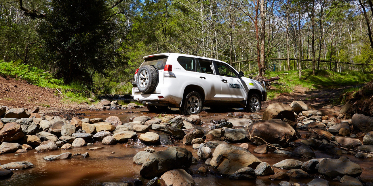 Ranger four-wheel drive vehicle crosses a shallow creek with rocks