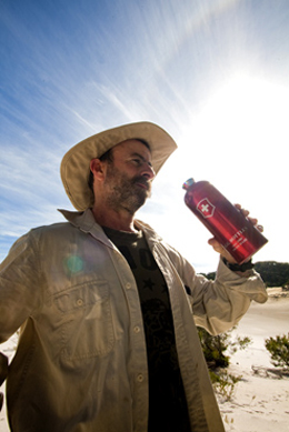 Photo of a walker drinking from a water flask with glaring sun behind him.
