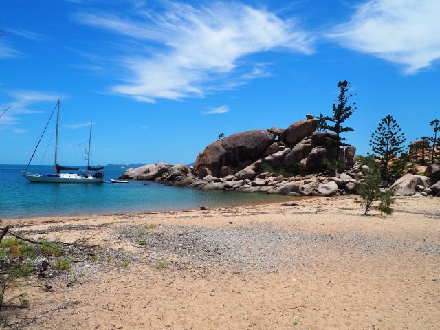 Photo of Arthur Bay beach, with blue skies and blue water, a boat anchored and large boulders just on the shore.
