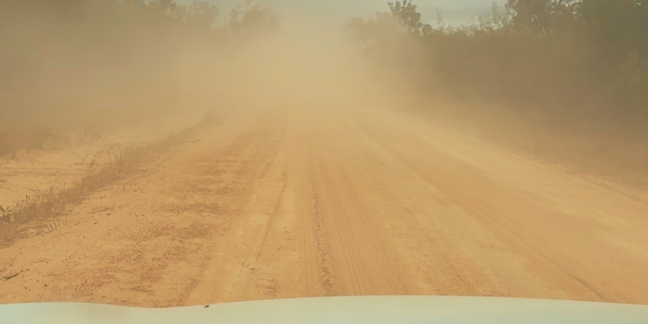 View from vehicle of dirt road clouded with orange dust