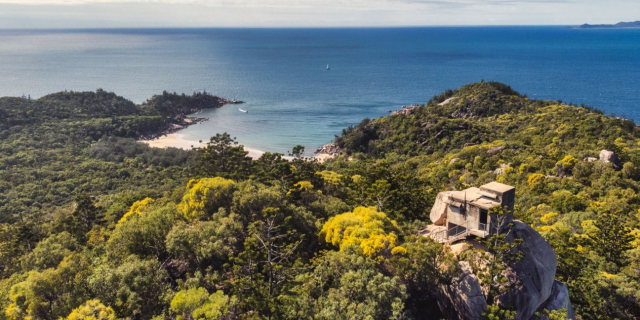 A panorama of Magnetic Island showing the vegetation covering over 75% of the island, with a stretch of white sand and clear blue waters beyond