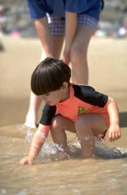 Child playing in the shallow water, with adult right behind them.