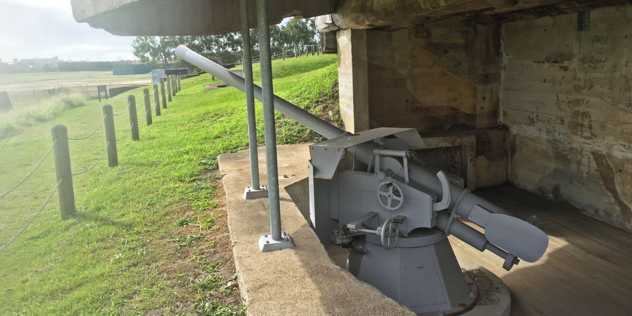 Grey naval gun relic mounted in a concrete bunker.