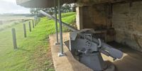 Grey naval gun relic mounted in a concrete bunker.