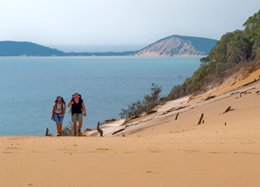 Photo of two people walking up the Carlo Sand Blow with the ocean and islands in the background.