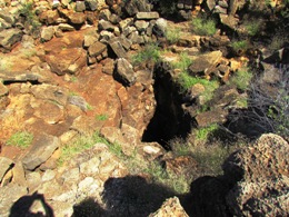 Looking down into the vertical shaft of a sinkhole. Numerous rocks and boulders on the edge with a deep dark cave shaft.