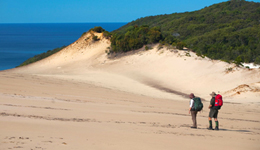 Photo of two walkers who look small with the large sandblow in the background.