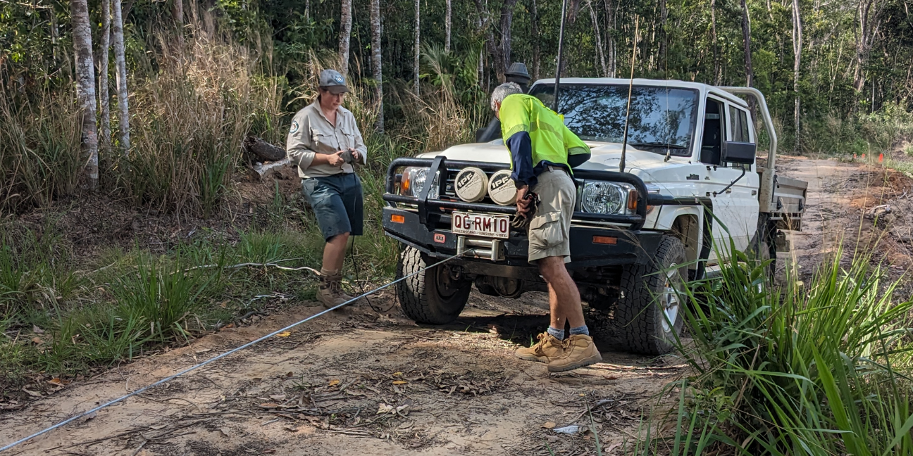 Four-wheel drive vehicle being winched by Ranger and saftey person standing next to vehicle