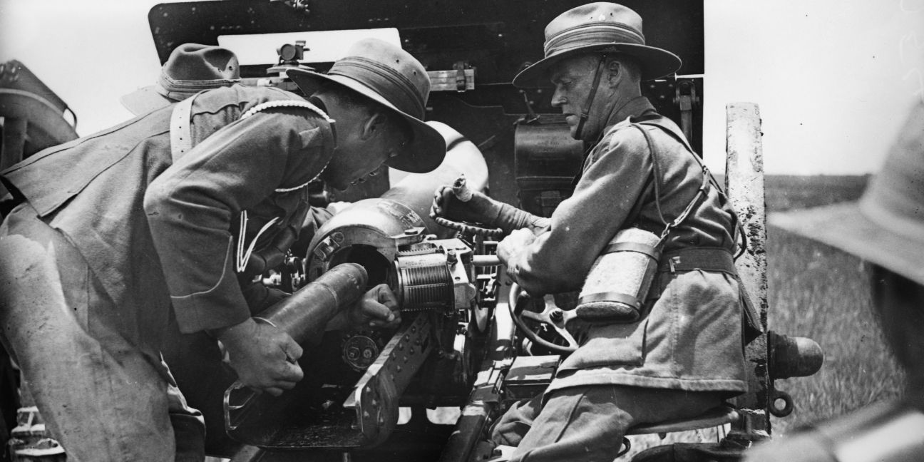 Black and white image of two men in military uniforms loading a shell into an artillery gun.