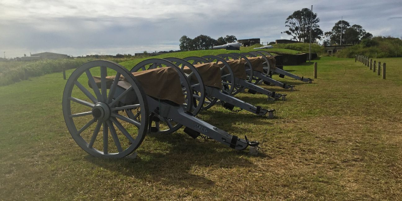 Five artillery guns lined up on a grassy hill.