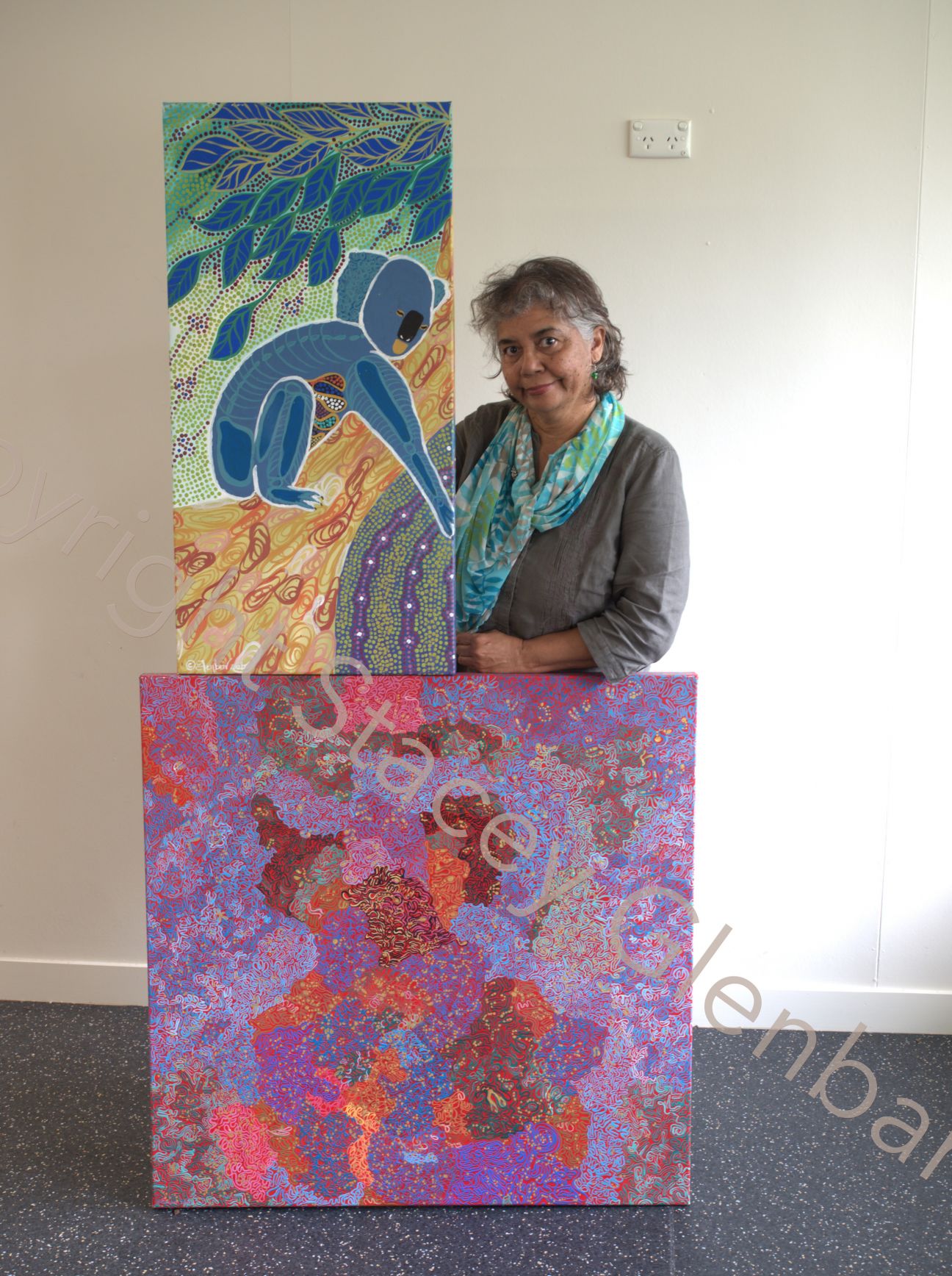 Wulgurukaba woman standing with two pieces of Aboriginal style artwork.